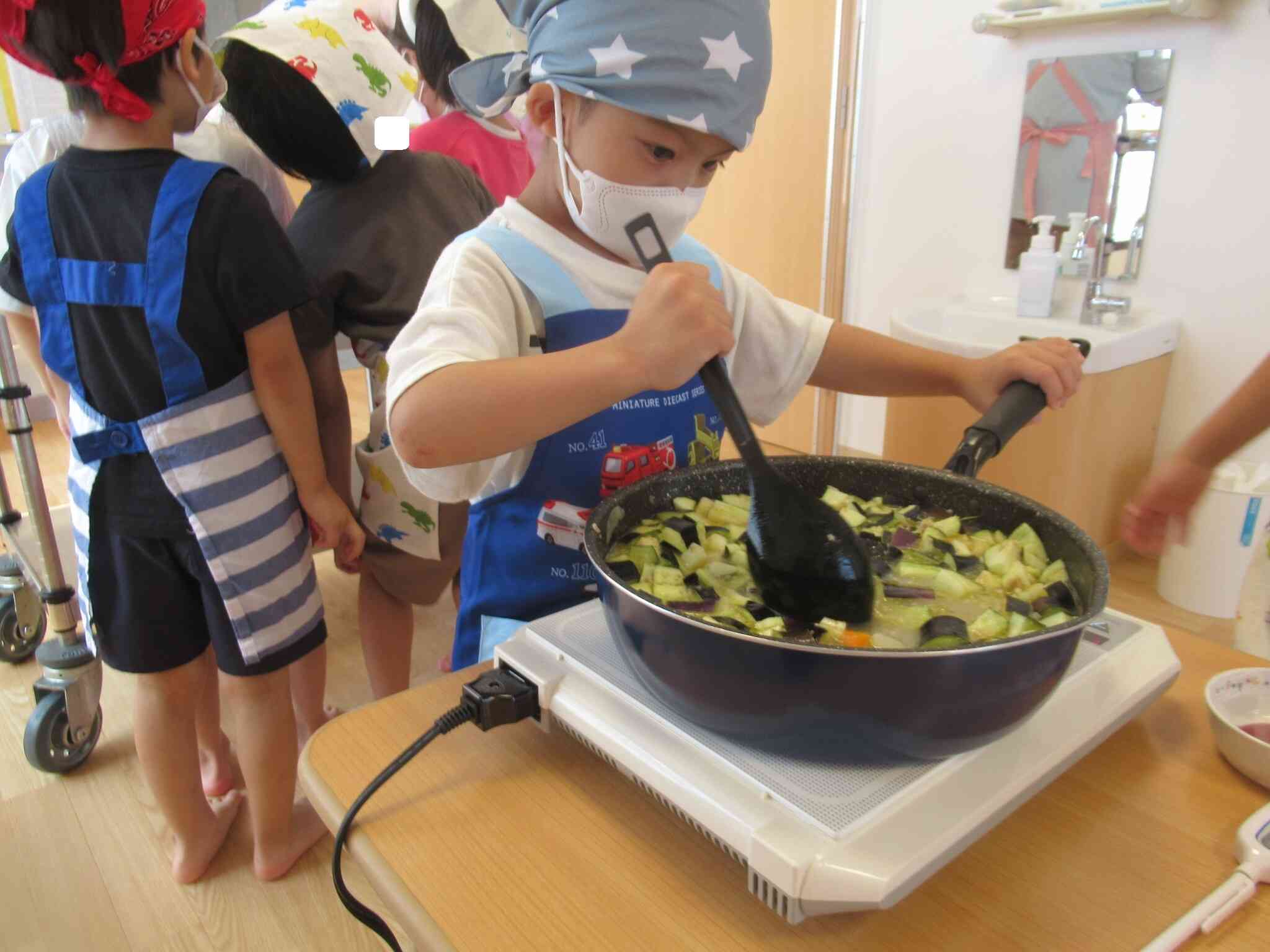 ナスも追加して、混ぜます…フライパンの取っ手をもってこぼさないように真剣なまなざしです