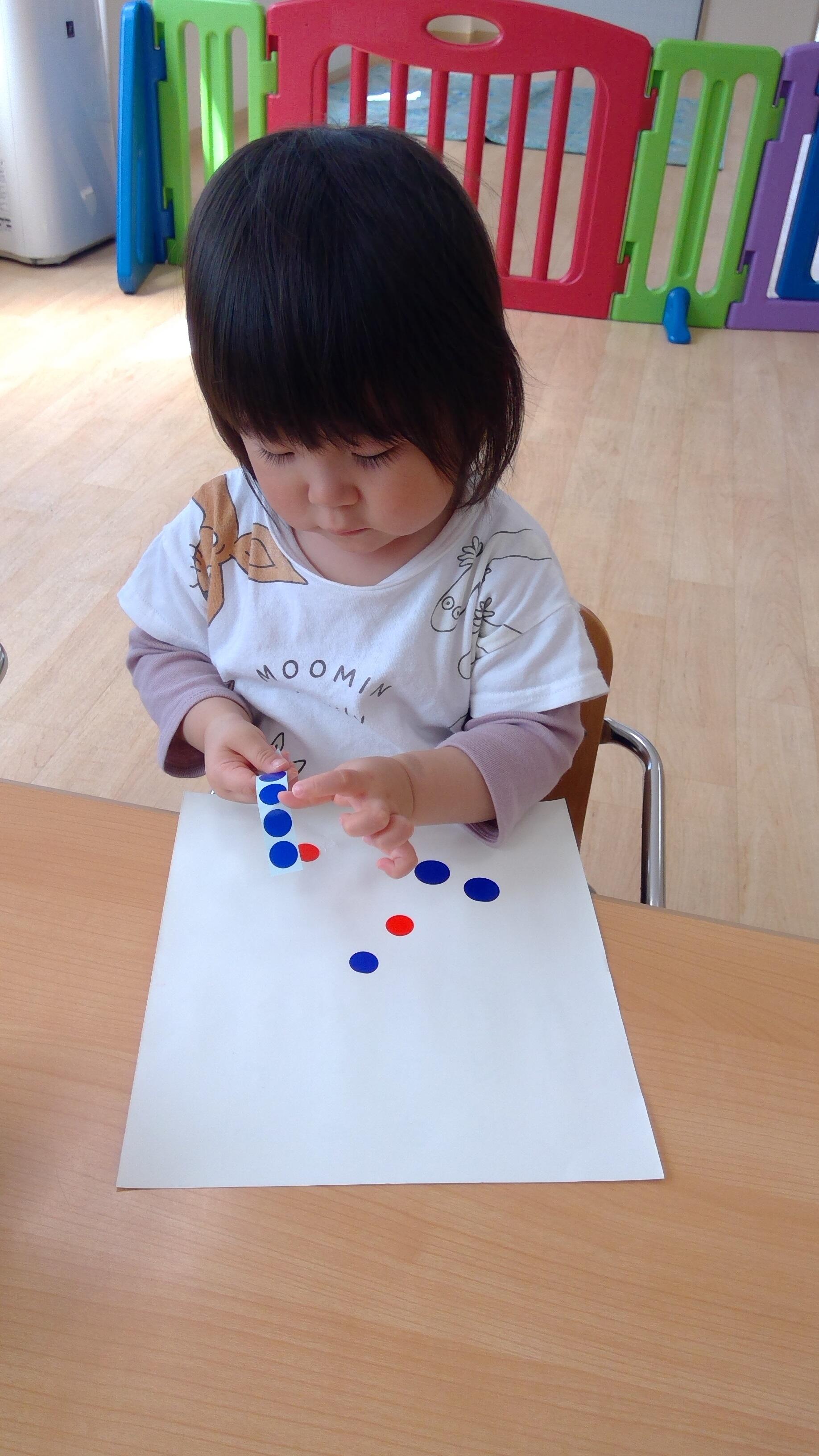 １歳児クラス、この日はシール貼りをしています。台紙から上手にシールを剥がしています。