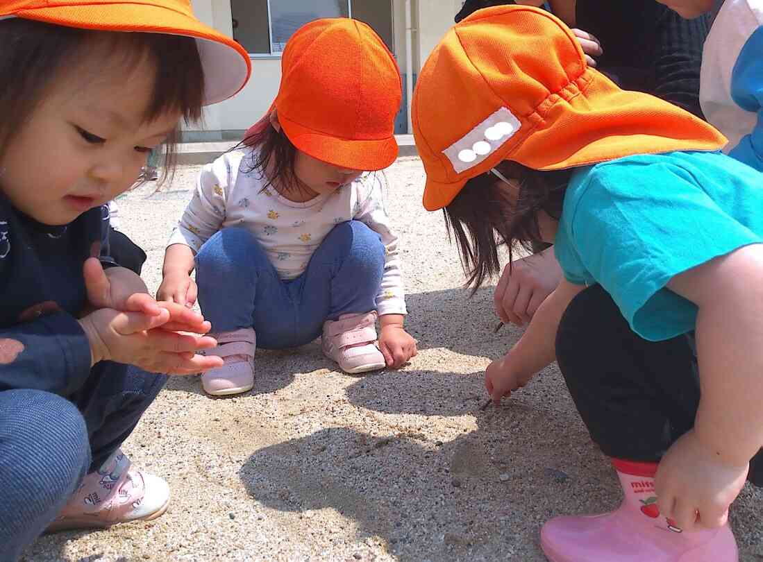 保育士が落ちていた枝を拾って土にみんなが大好きなキャラクターの絵を描くと、子どもたちも真似をして描いていました。何の絵を描いているのかな？