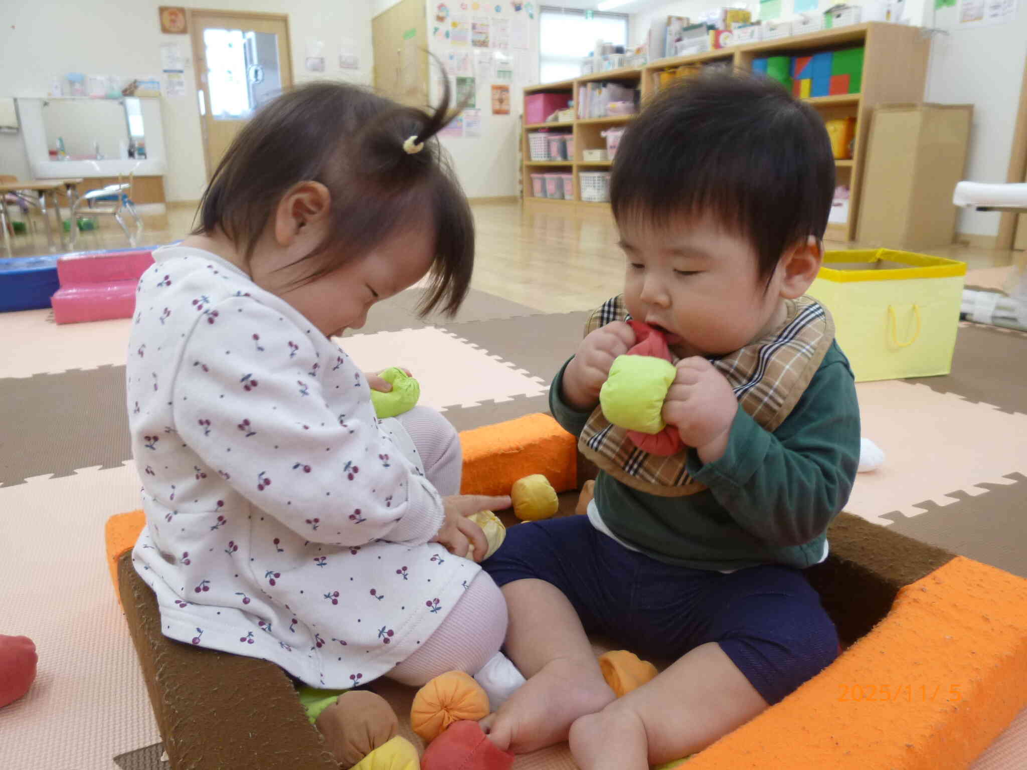 ０歳児のお友だちがロの字に入ってまるでプールみたい♡お手玉を握ったり、頭にのせたり...と思い思いの遊び方で楽しんでいました。2人のほっこりした様子をパシャリ☆顔がほころぶ先生でした。