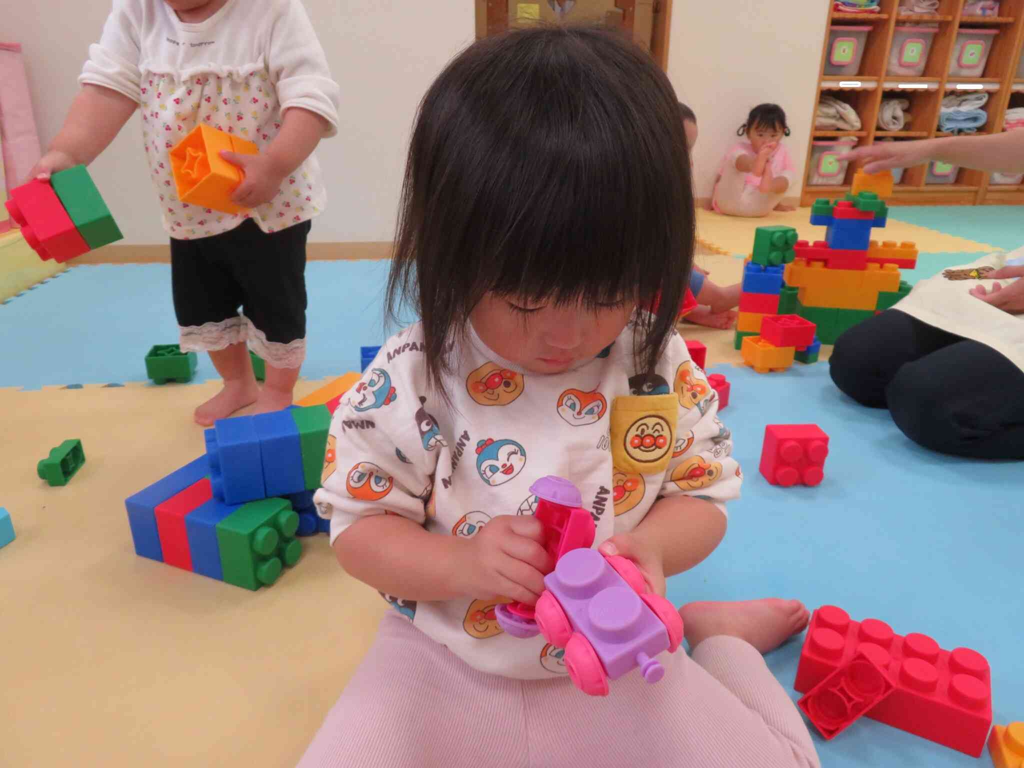 タイヤのついた車のようなパーツも加わり、「どうやってくっつけるのかなあ・・」2歳児Mちゃん集中。すぐにできない！って助けを呼ぶ前に、自分でどうにかしてみようって頑張れるようになっています。