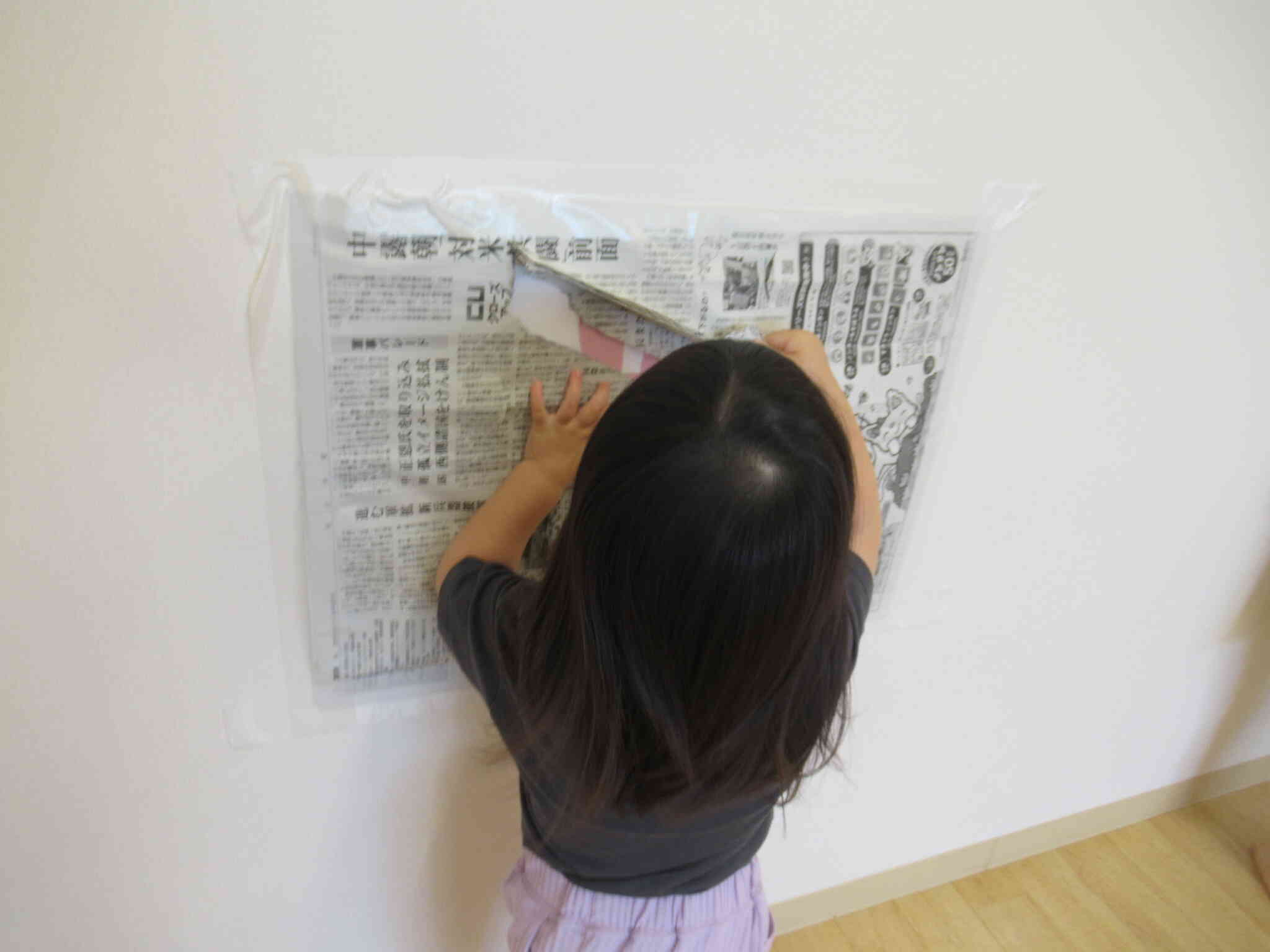 壁に貼っている新聞紙を破いています。