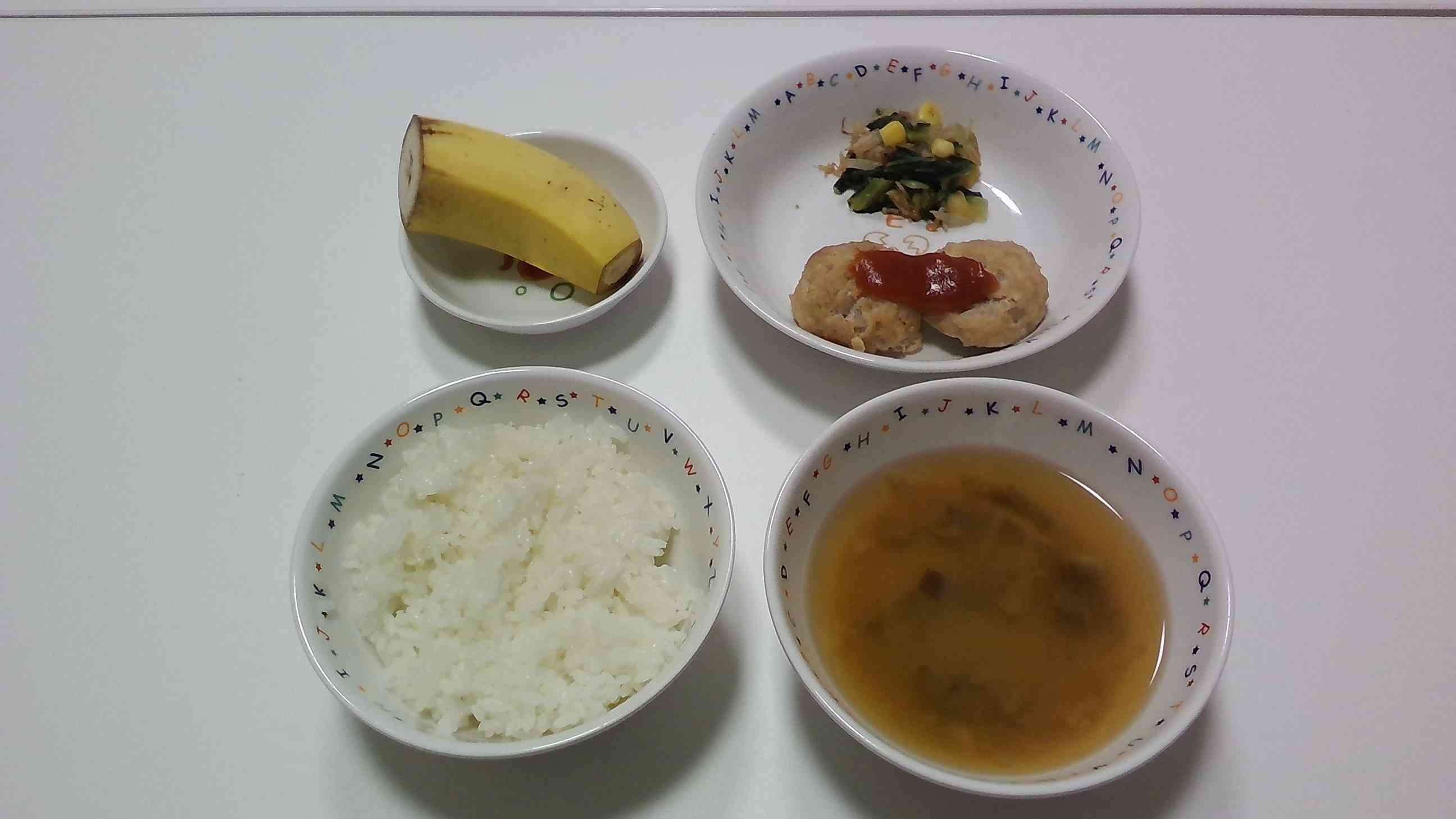 ごはん、なすのお味噌汁 豆腐ハンバーグ こまつなのおかかあえ　バナナ。水切りをした豆腐と豚挽を使ってふんわりと やわらかい食感は子どもたちにも食べやすい メニューです。たんぱく質がしっかり 摂れるバランスのよい一品です 。