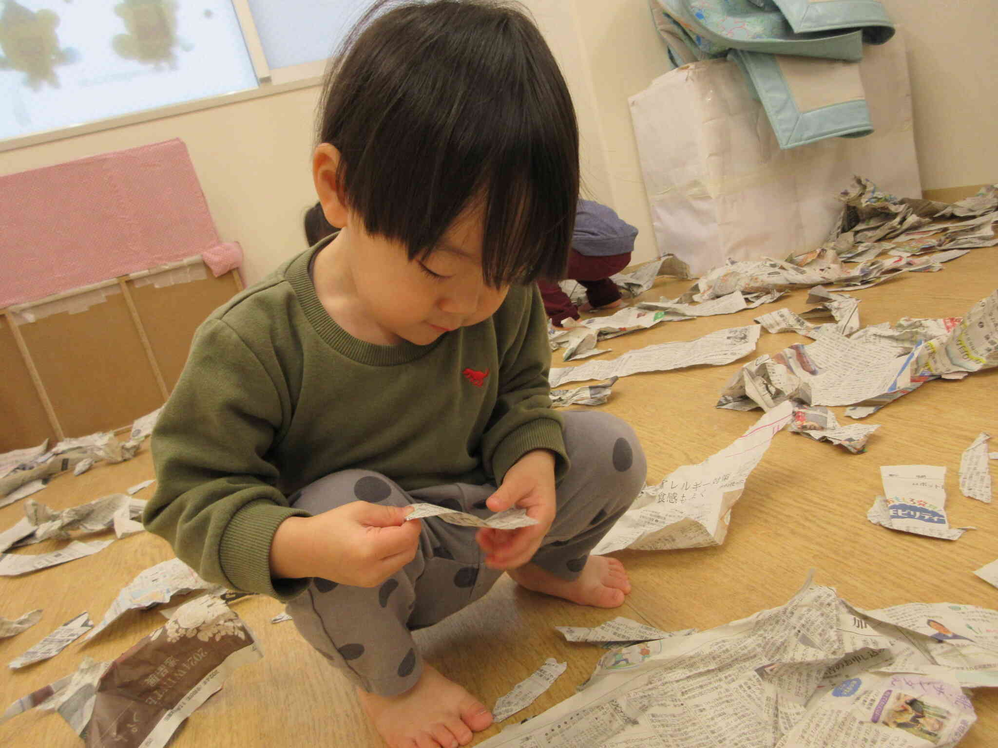 新聞紙に載っている写真やイラストが気になっている様子。「せんせー、何これ？」と興味津々です。