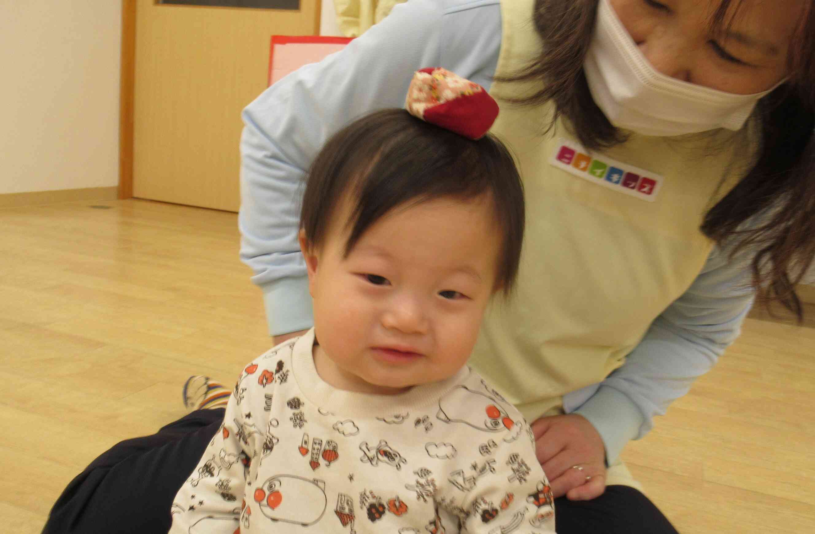先生にお手玉を頭にのせてもらいじっとしている0歳児Tくん。上手じょうず!