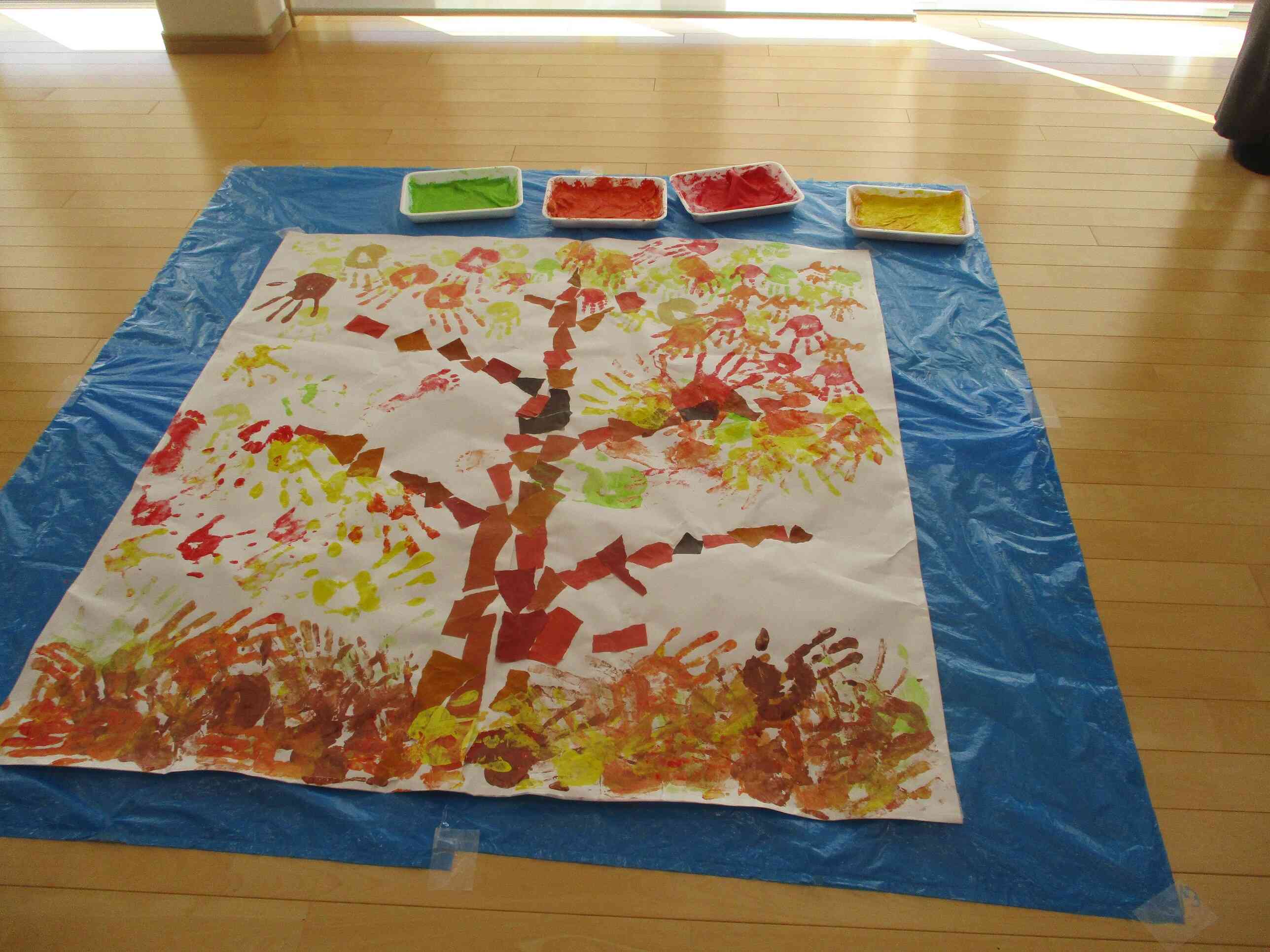 もうすぐ完成！土台となる部分は先生たちの手型です。お父さんやお母さんの大きな手と子どもたちの小さな手がいい感じに混ざり合っています。