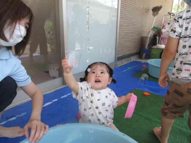 お水が落ちていくのをカップで受け止めようと手を伸ばすひよこ組のＴちゃん。