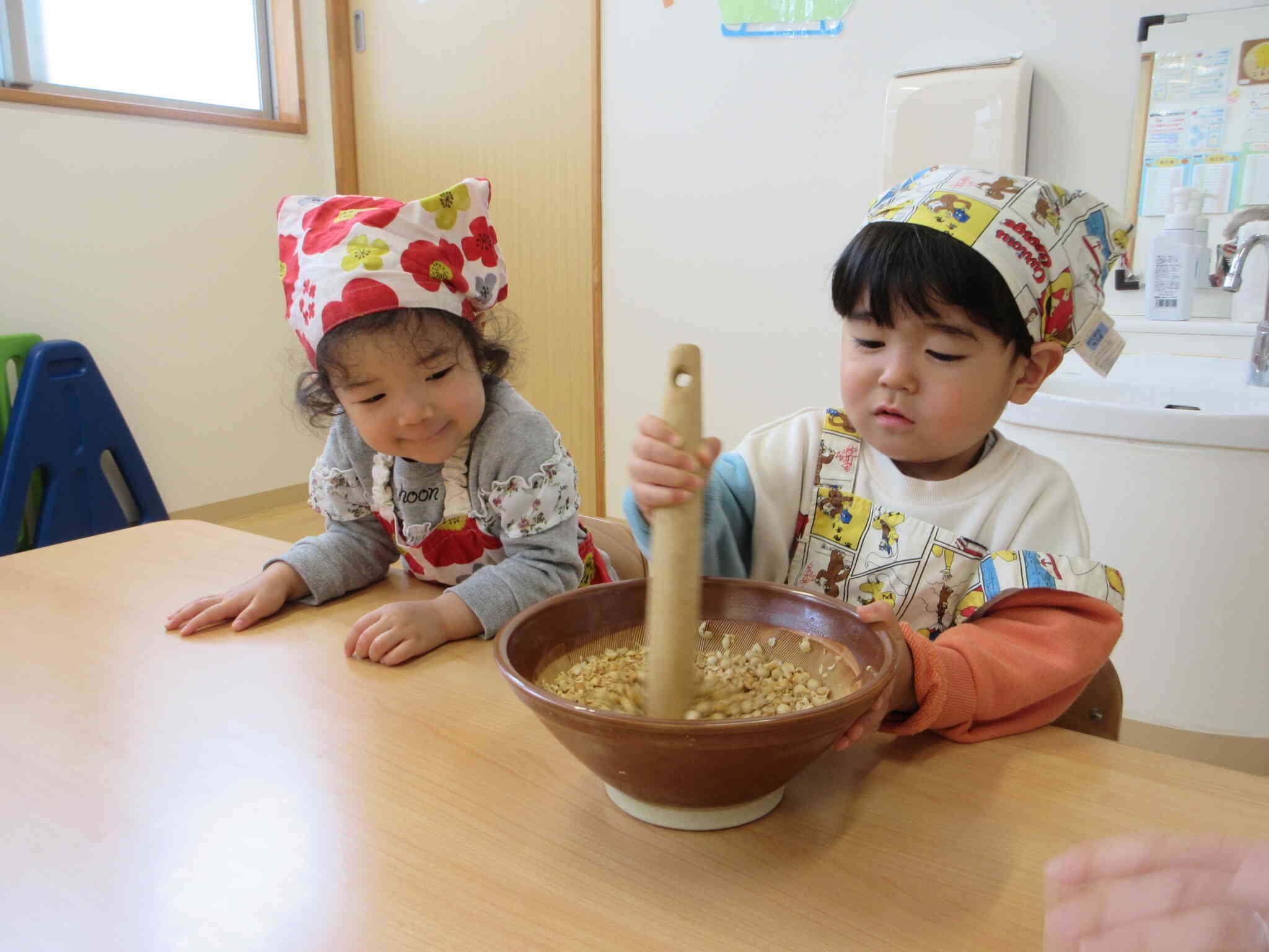 真剣な表情ですりこぎで大豆をつぶしているSくんとその様子をニコニコで見ているRちゃん