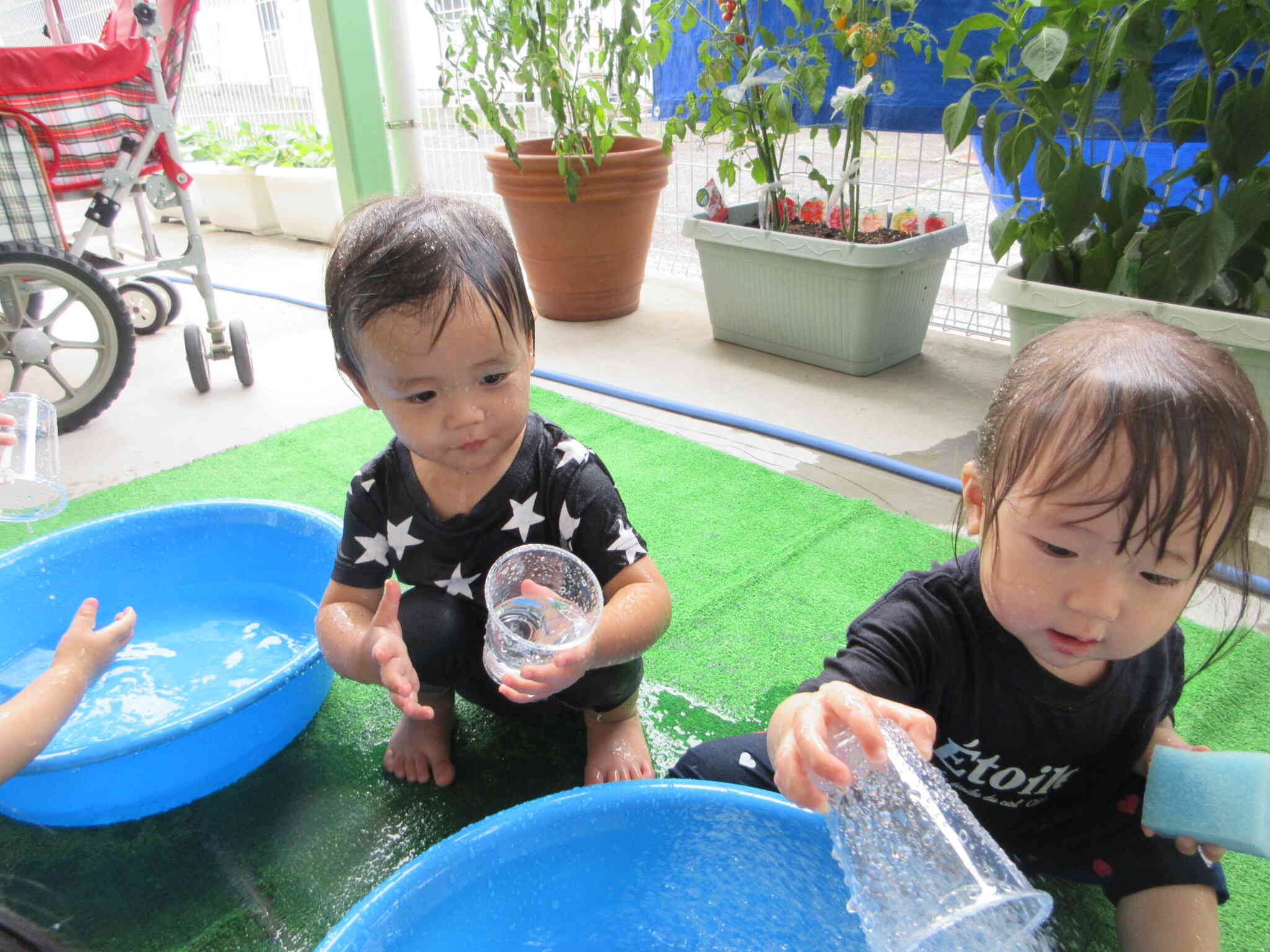 「せんせい、どうぞ」とカップを手渡すRちゃんとカップで水をすくって楽しんでいるYくん